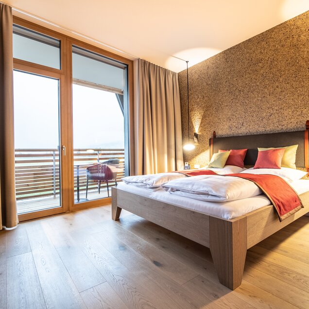 Bright hotel room with double bed, wooden floor, balcony and patterned wall