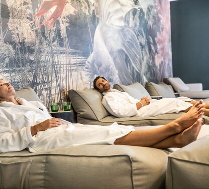 Relaxed people in bathrobes lying on loungers in a lounge with a mural