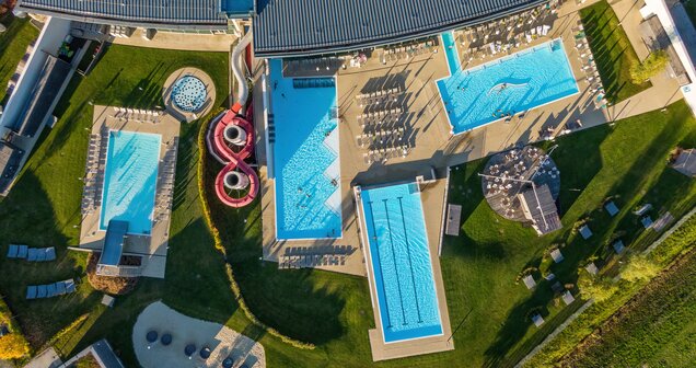 Aerial view of a thermal spa with swimming pools, sunbathing areas, slides and green spaces