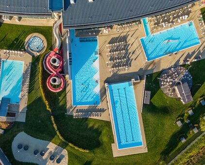 Aerial view of a thermal spa with swimming pools, sunbathing areas, slides and green spaces