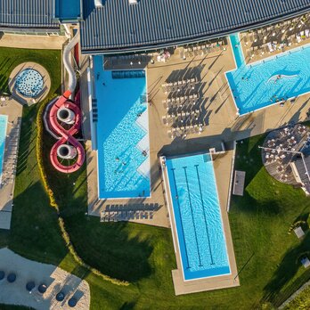 Luftaufnahme einer Therme mit Schwimmbecken, Liegeflächen, Rutschen und Grünflächen