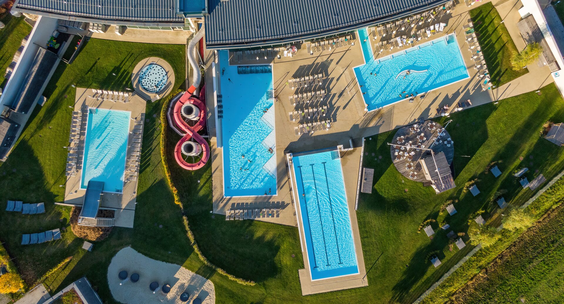 Luftaufnahme einer Therme mit Schwimmbecken, Liegeflächen, Rutschen und Grünflächen