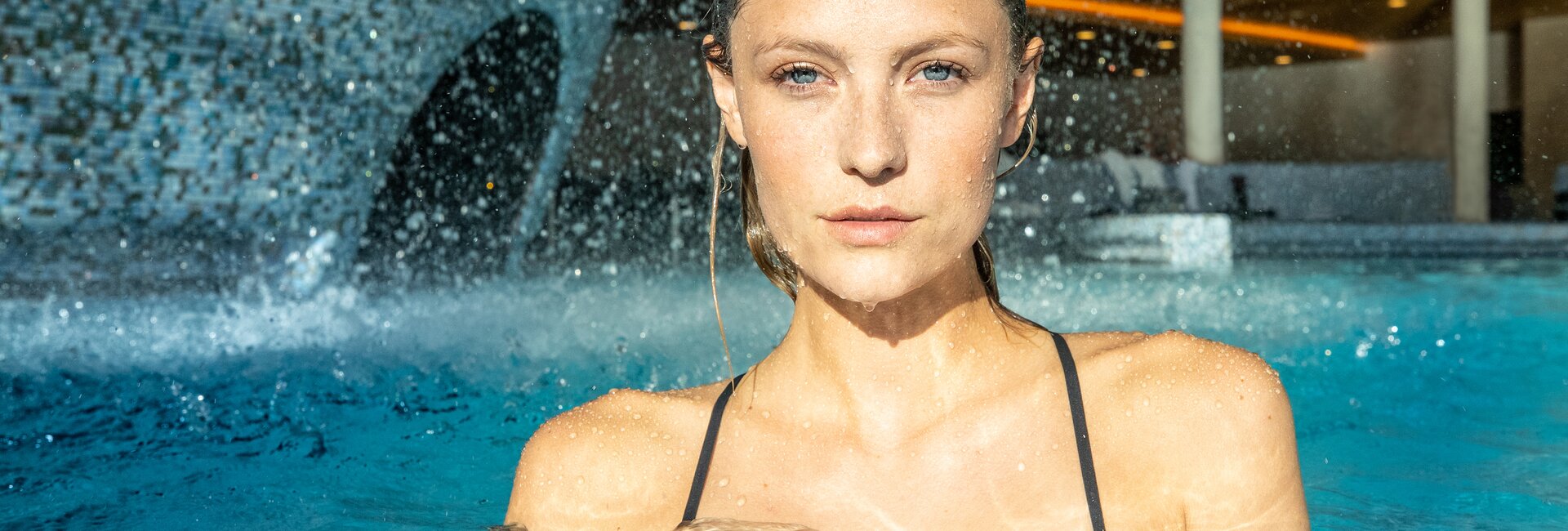 Frau im Schwimmbad vor Wasserfall mit Blick in die Kamera