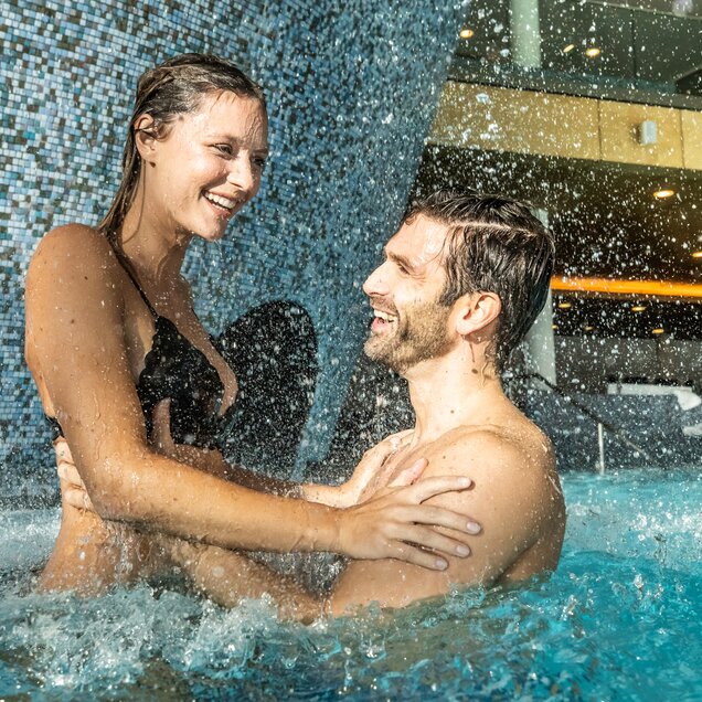 Laughing couple in the swimming pool under a waterfall