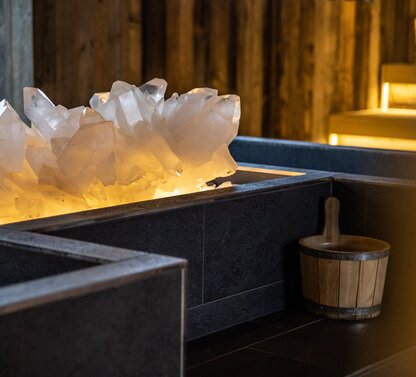 Detail of rock crystal in dark basin next to wooden bucket in sauna area