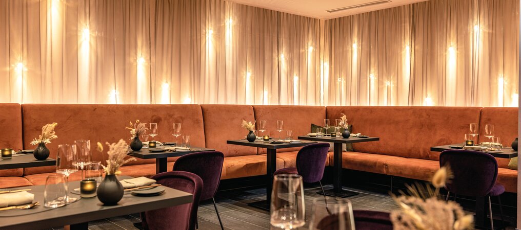 Restaurant mit gedeckten Tischen, orangefarbener Eckbank und violetten Stühlen