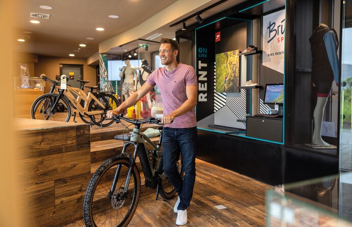 Mann schiebt E-Mountainbike in Fahrradverleih mit Aufschrift Rent