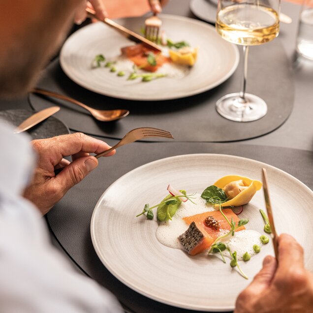 Person eating salmon and tortelloni on a plate with white sauce and herbs