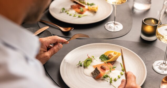 Person eating salmon and tortelloni on a plate with white sauce and herbs