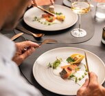 Person eating salmon and tortelloni on a plate with white sauce and herbs