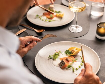 Person eating salmon and tortelloni on a plate with white sauce and herbs