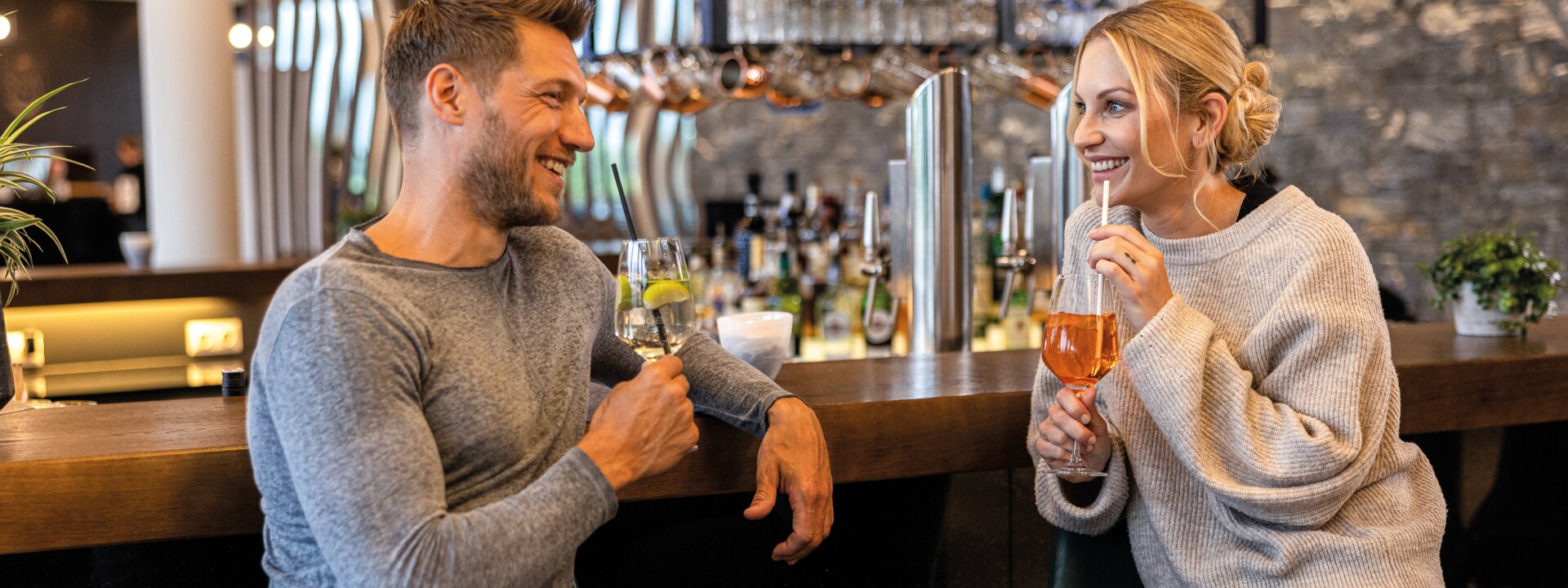 Lachendes Paar sitzt an Hotelbar mit Cocktails in der Hand