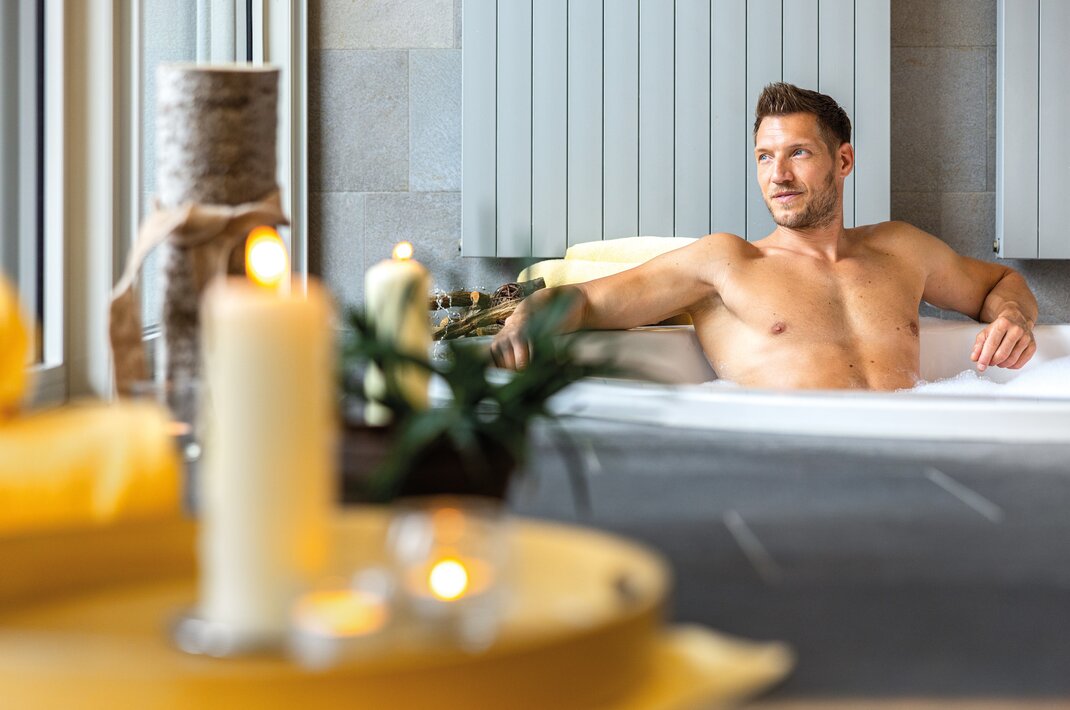 Oberkörperfreier Mann entspannt in Badewanne mit Kerzen im privaten Spa