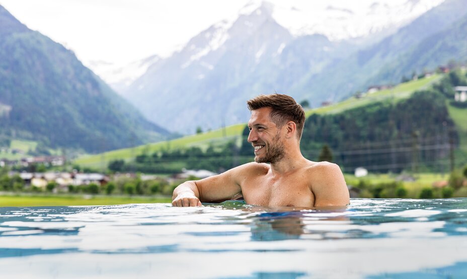 Lachender, oberkörperfreier Mann im Pool vor Bergpanorama