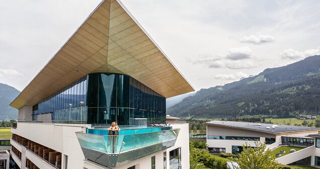 Frau im Skylinepool auf Hoteldach mit Glasfront vor Bergpanorama
