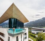 Frau im Skylinepool auf Hoteldach mit Glasfront vor Bergpanorama
