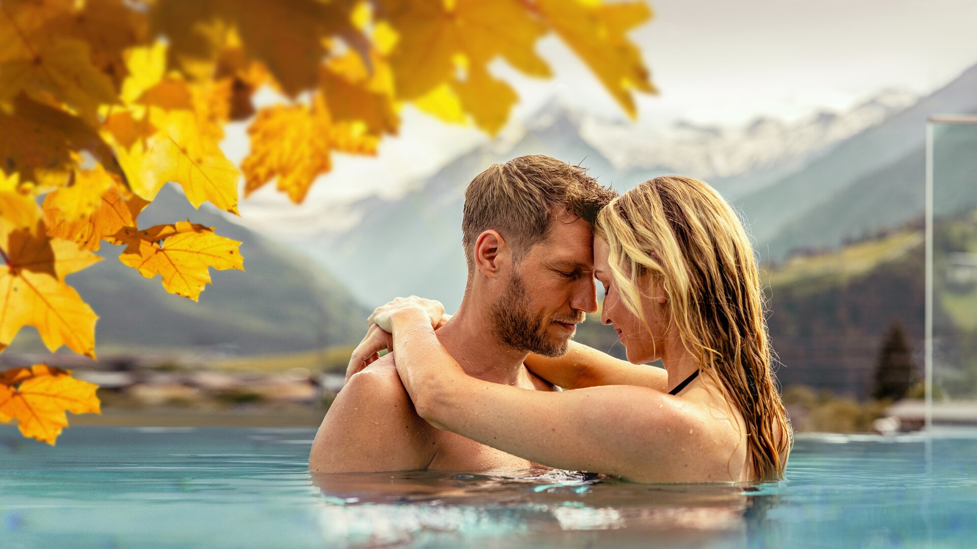 Couple hugging in the water against a backdrop of mountains and autumn leaves