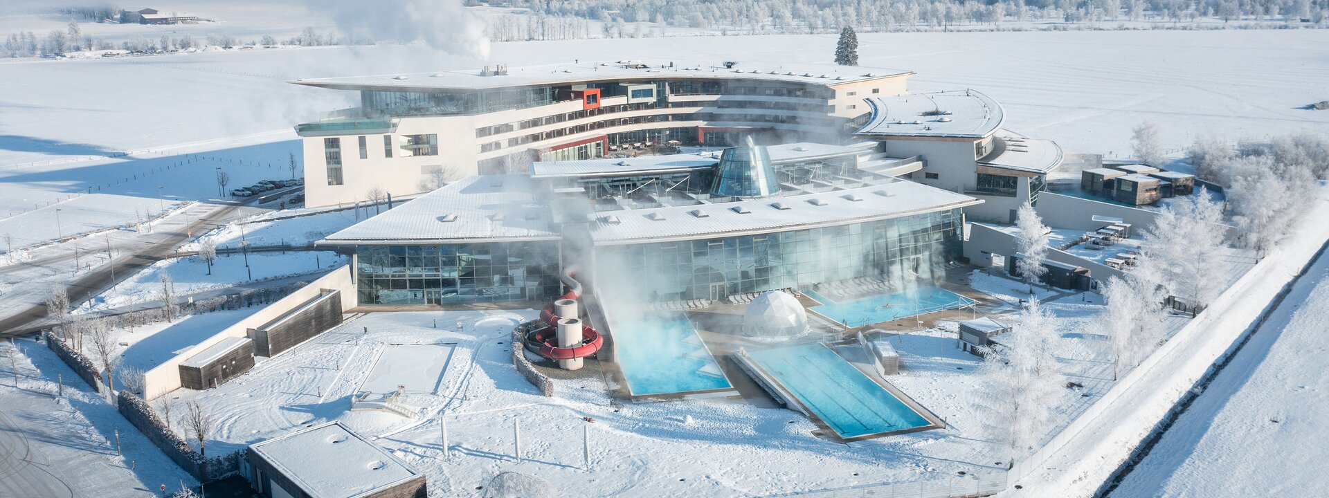 Aerial view of a thermal spa in winter with snow-covered landscape and mountains in the background