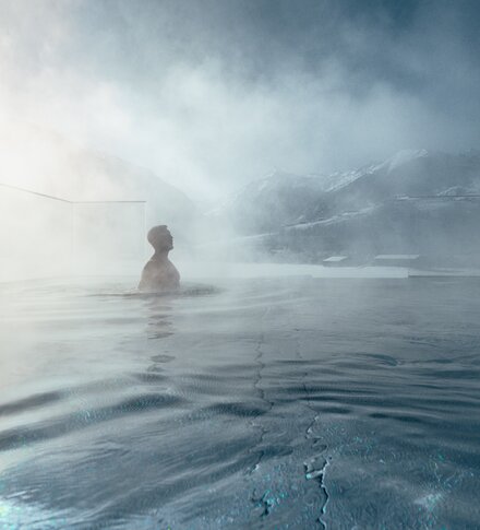 Person im dampfenden Glas-Panoramapool vor verschneiter Winterlandschaft