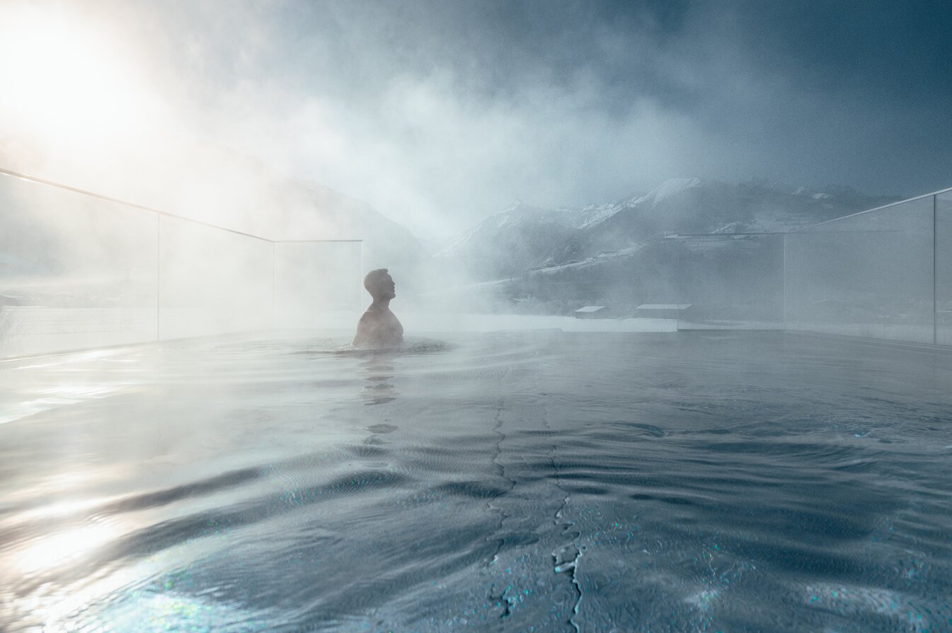 Person in steaming glass panoramic pool in front of snowy winter landscape