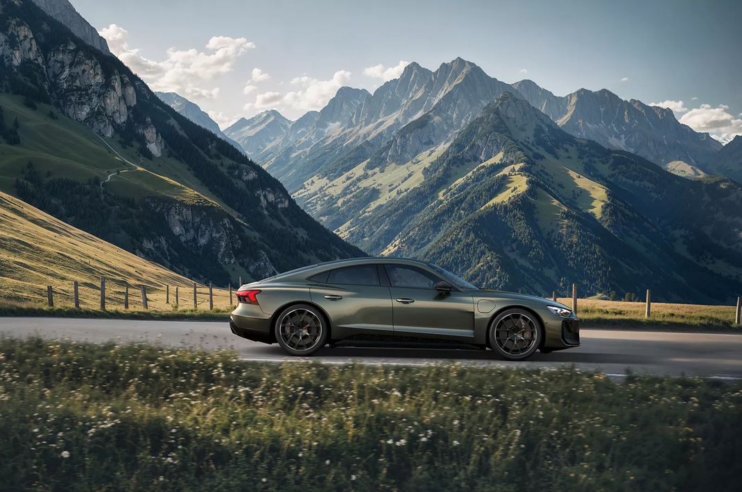 Dunkelgrünes Sportauto auf Bergstraße vor Alpenkulisse
