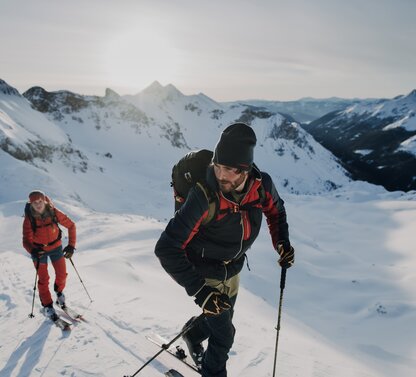 Skitourengeher steigen mit Skiern und Stöcken einen schneebedeckten Hang hinauf Bergpanorama im Hintergrund