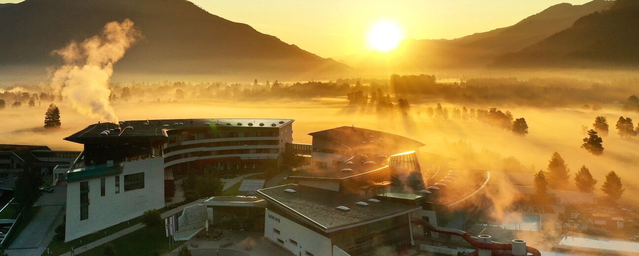 Resort im Herbstnebel bei Sonnenaufgang vor Bergkulisse