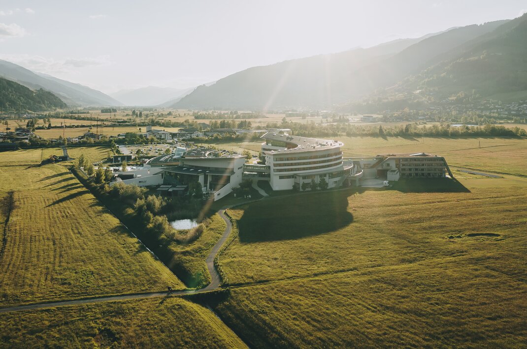 Luftaufnahme eines modernen Hotels in grüner Landschaft vor Bergen