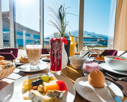 Set breakfast table with drinks, fruit, cheese, egg and view from the window