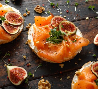 Bruschetta mit Lachs, Feigen und Frischkäse auf dunklem Holztisch mit Nüssen und Sprossen