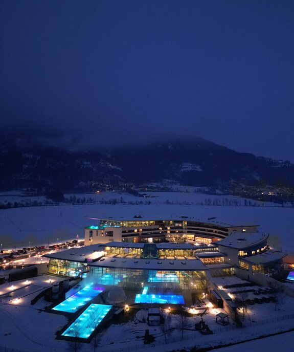 Therme im Schnee bei Nacht mit beleuchteten Pools und Bergen im Hintergrund