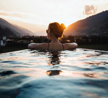 Frau im Pool mit Blick auf Berge bei Sonnenuntergang