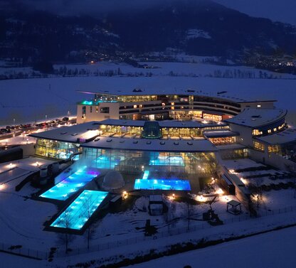 Thermal spa in the snow at night with illuminated pools and mountains in the background