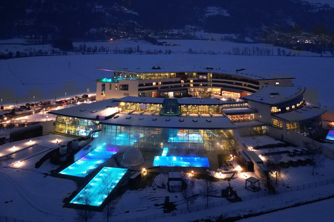 Therme im Schnee bei Nacht mit beleuchteten Pools und Bergen im Hintergrund