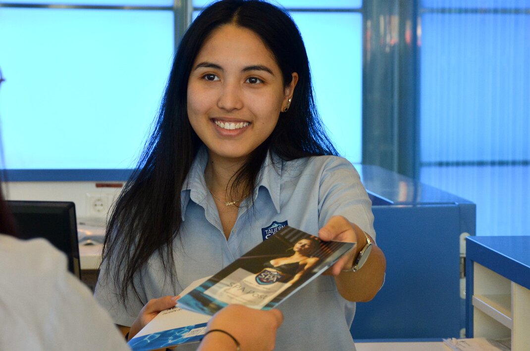 Lächelnde Mitarbeiterin übergibt Broschüre an Kunden