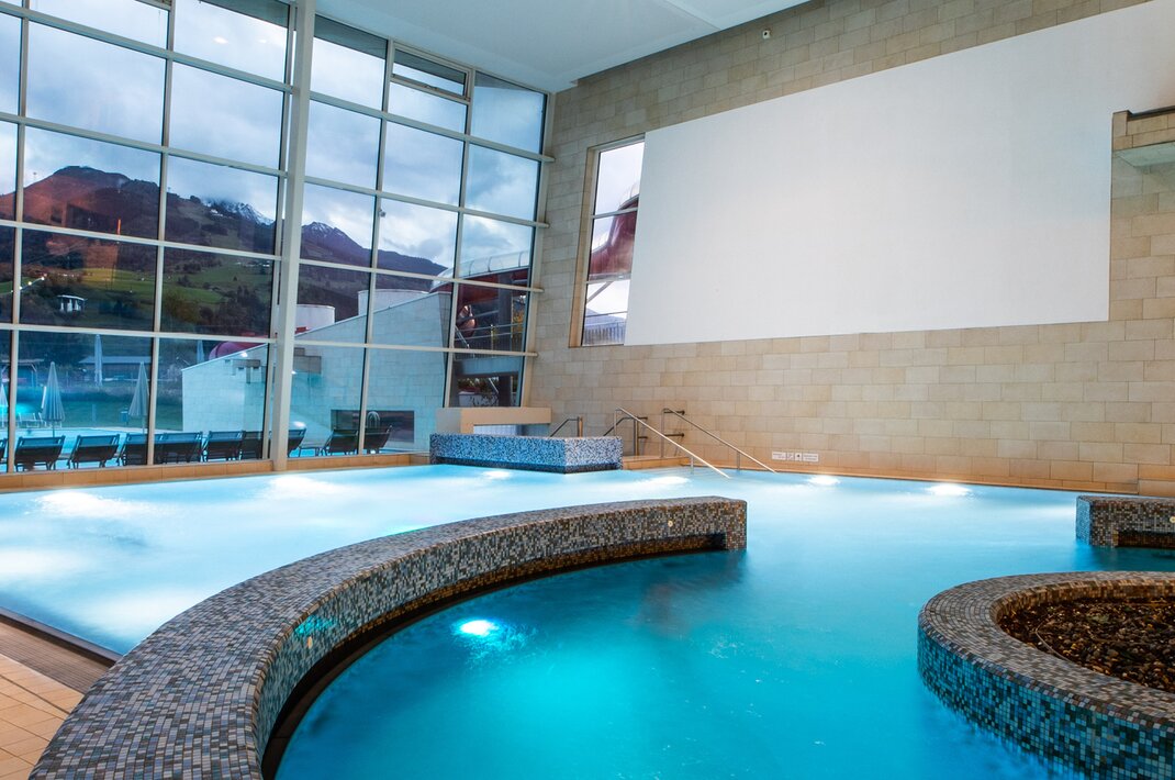 Beleuchteter Innenpool mit Alpenpanorama und Glasfassade