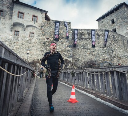 Mann mit Kette läuft bei Winter Spartan Race vor Burg
