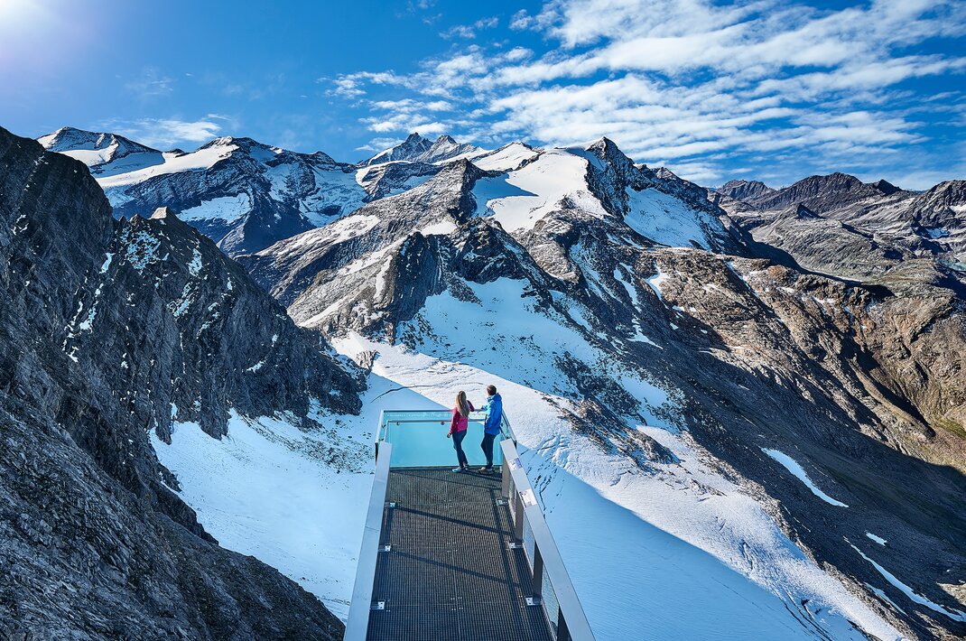 Paar auf Aussichtsplattform vor schneebedeckten Bergen im Nationalpark Hohe Tauern