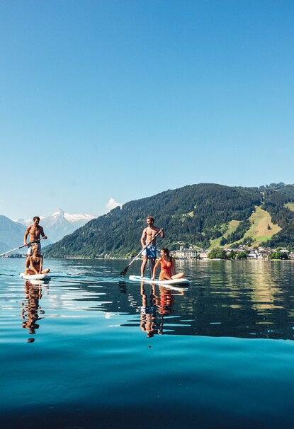 Menschen paddeln auf Stand-Up-Paddleboards auf einem See vor Bergkulisse