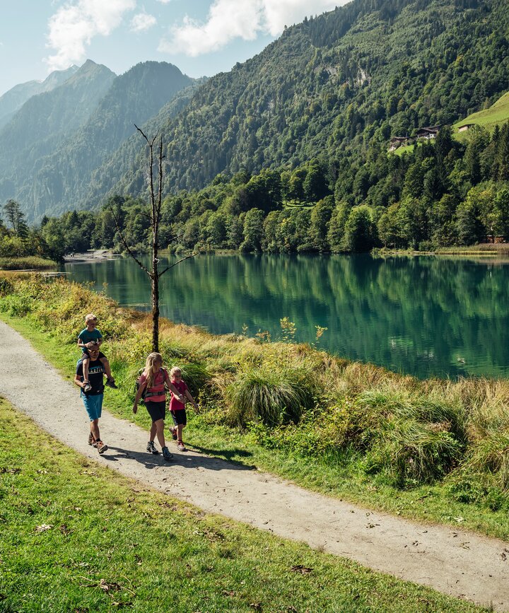 Familie wandert am Klammsee entlang, im Hintergrund Berge und Wald