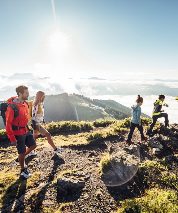 Familie wandert auf Bergpfad mit Blick auf bewaldete Hügel und Wolkenfelder