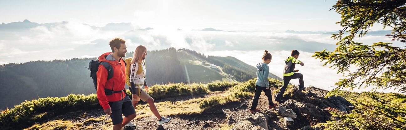 Familie wandert auf Bergpfad mit Blick auf bewaldete Hügel und Wolkenfelder