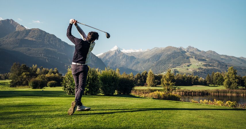 Golfer beim Abschlag auf Grün vor Bergpanorama