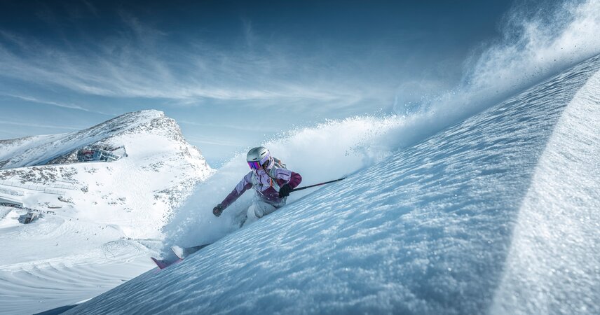 Dynamischer Skifahrer auf verschneiter Piste unter blauem Himmel