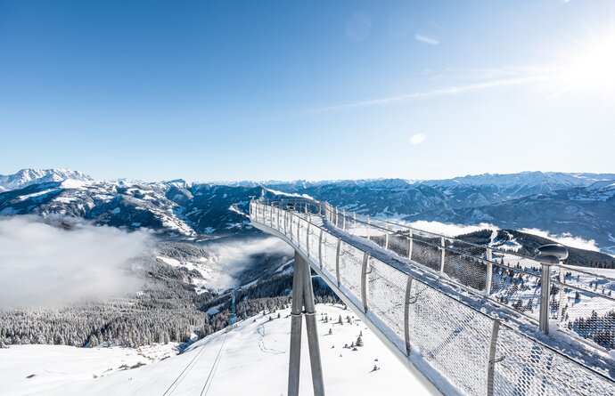 Schneebedeckter Skywalk über winterlicher Berglandschaft mit Wolken