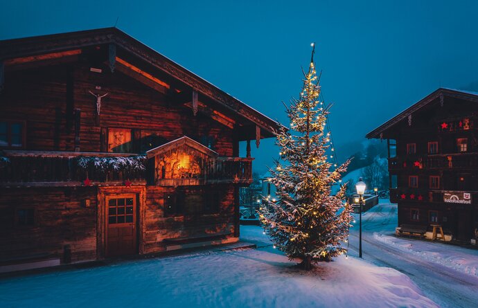 Verschneites Holzhaus neben beleuchtetem Weihnachtsbaum im Advent