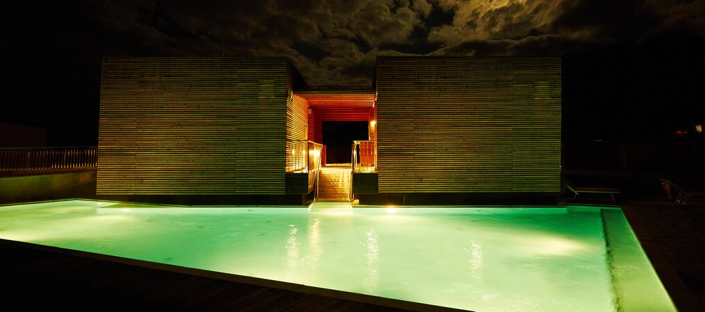 Grünlich beleuchteter Pool unter nächtlichem Mondhimmel