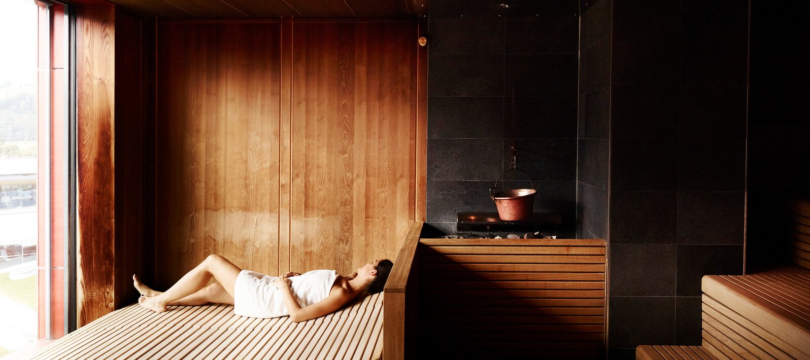 Frau liegt entspannt in Sauna mit Holzverkleidung