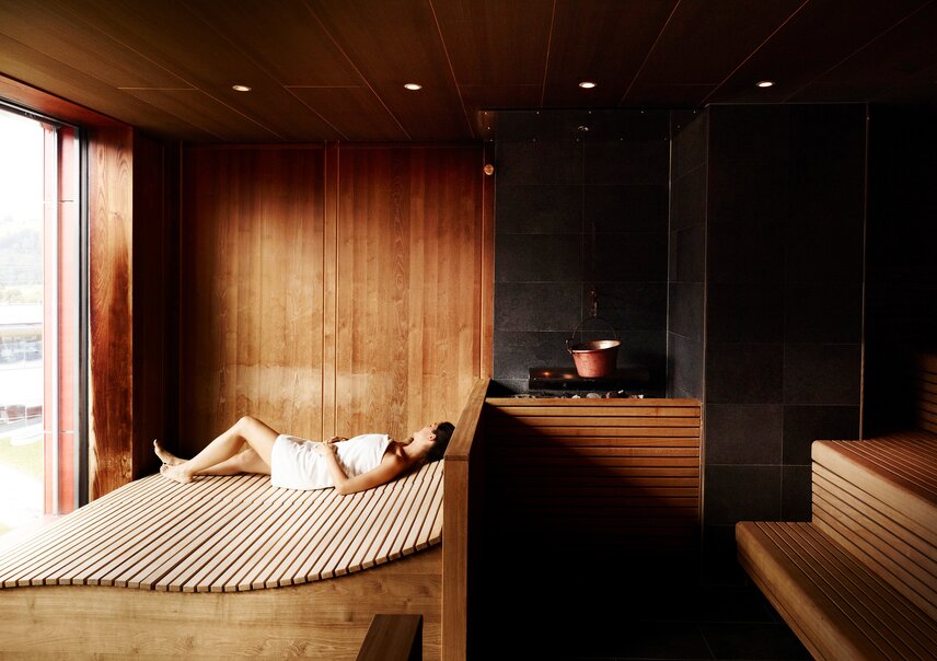 Frau liegt entspannt in Sauna mit Holzverkleidung