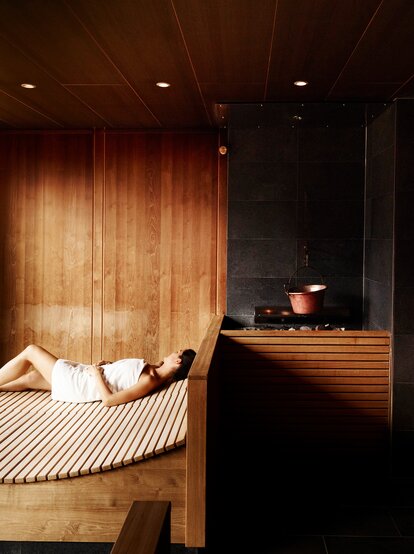 Frau liegt entspannt in Sauna mit Holzverkleidung